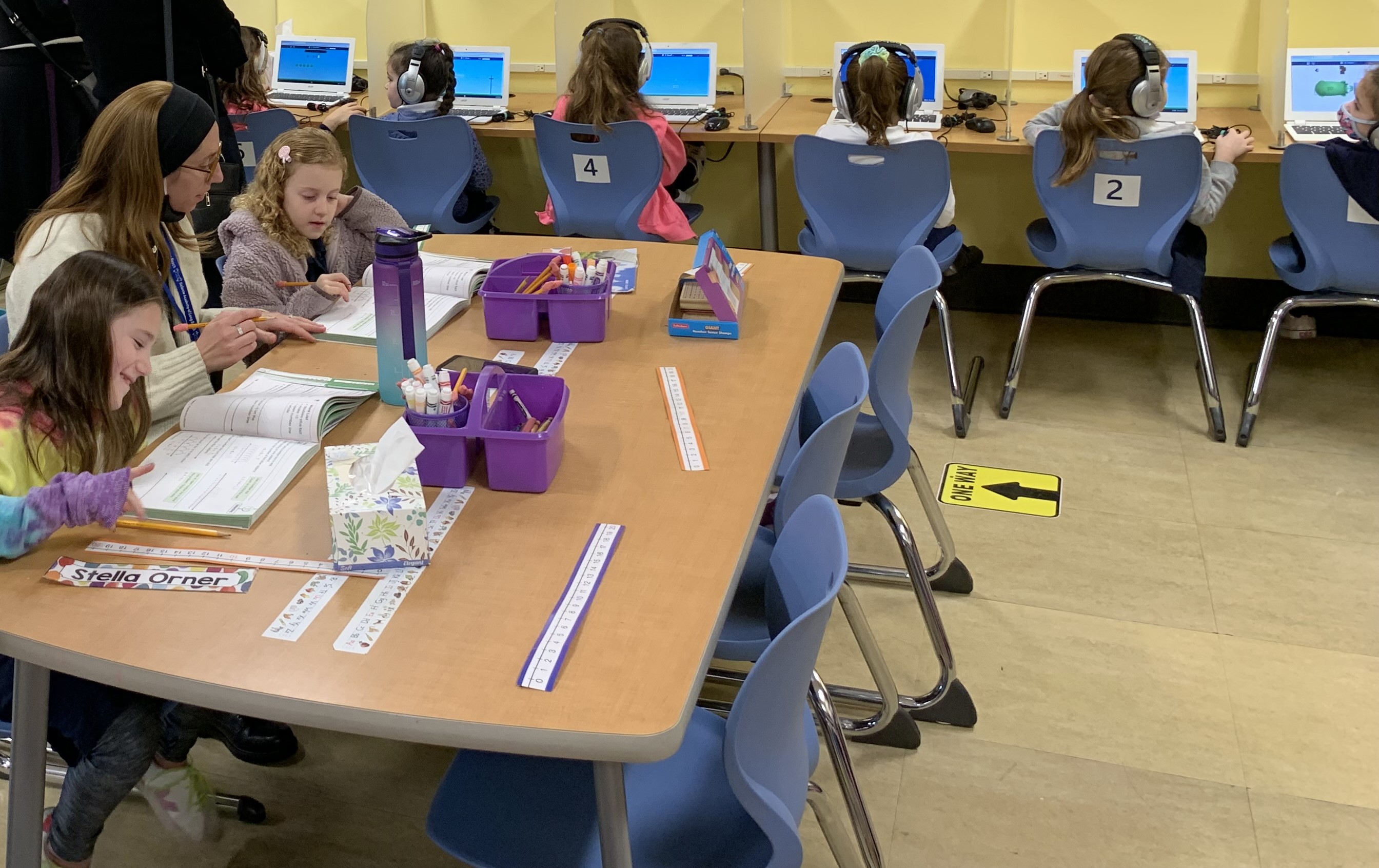 A teacher works with a small group while other students learn on computers